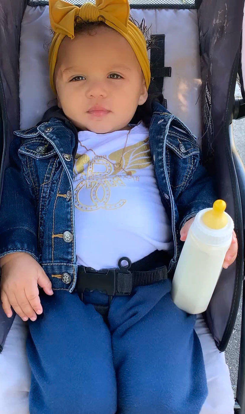 Maelani is registered to the contest to win money with this photo: baby, baby_carriage, baby_safety, baby_toddler_clothing, beauty, bottle, cheek, child, collar, electric_blue, eye, happy, headwear, outerwear, person, plastic_bottle, sitting, skin, sleeve, toddler