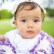 Tiana is registered to the contest to win money with this photo: baby, child, flower_crown, blanket, purple, white, outdoor, portrait, closeup, cute, infant, face, soft_focus, nature, greenery, young, innocent, headwear, expression, curious