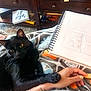 animal, arm, black_cat, blanket, books, cat, cozy, cup, desk, drawing, hand, indoor, line_art, paw, person, pet, relaxing, sketchbook, tattoo, wooden_furniture