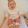 baby, barefoot, blanket, changing_table, child, cute, floral_clothing, furniture, happy, indoor, infant, person, pigtails, pink_pants, portrait, room, sitting, smiling, soft_lighting, wooden_frame