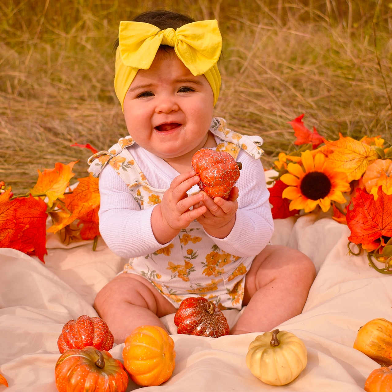 Maielynn joined the competition — help win amazing prizes! autumn_leaves, baby, blanket, child, cute, decor, fall, floral_overalls, grass, happy, headband, nature, outdoor, portrait, pumpkins, seasonal, sitting, smiling, sunflowers, yellow_bow