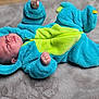 baby, child, infant, blue_onesie, dinosaur_costume, plush_blanket, crawling, cute, soft_texture, sleepwear, hooded_outfit, indoor, portrait, small_hands, lying_down, cozy, warm_clothing, adorable, expression, infant_face