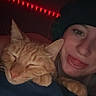 Milo is registered to the contest to win money with this photo: cat, person, beanie, orange_tabby, sleeping_cat, tongue_out, red_lights, nighttime, indoor, cozy, closeup, face, paw, blanket, resting, cute, pet, human, portrait, playful