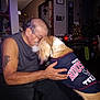 man, dog, indoor, affection, blur, tattoo, sleeveless_shirt, houston_texans, pet_clothing, embrace, home_decor, christmas_tree, wall_art, furniture, table, chair, lighting, person, animal, love