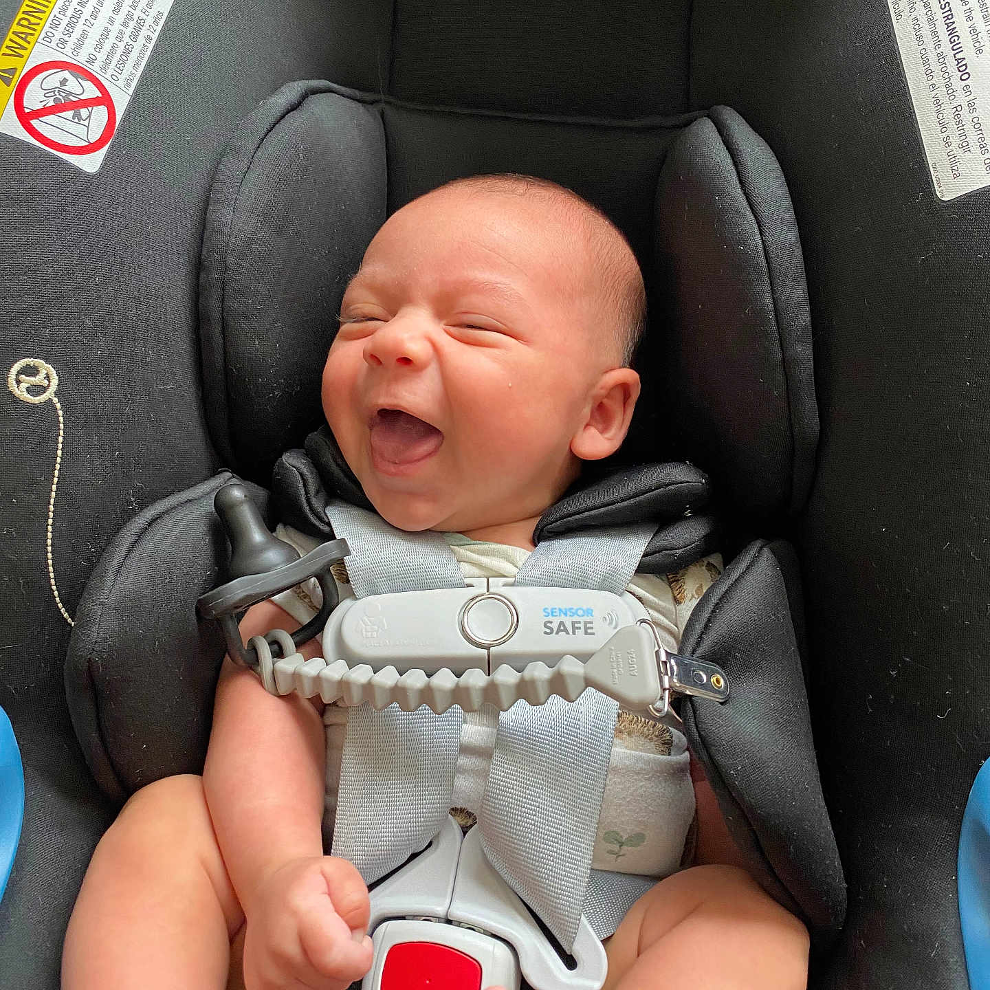 Grayson is registered to the contest to win money with this photo: baby, car_seat, child, clothing, cute, face, feet, happy, harness, indoor, infant, legs, newborn, pacifier_clip, person, safety, seat_belt, skin, smiling, warning_label