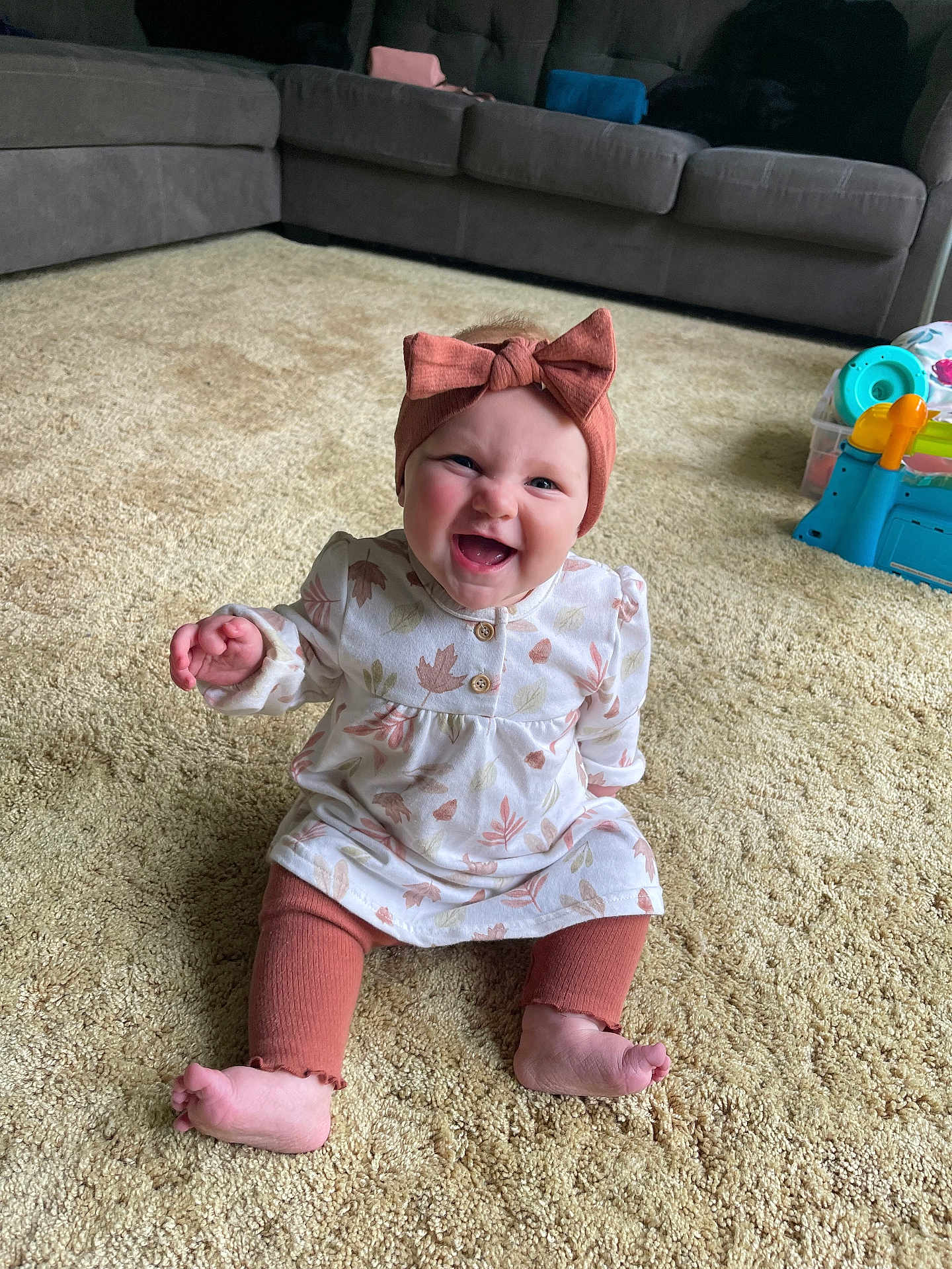Remington joined the competition — help win amazing prizes! baby, child, smile, happy, sitting, carpet, headband, bow, dress, leggings, living_room, sofa, toy, floor, indoor, person, cute, infant, expression, home