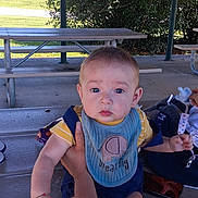Rovin joined the competition — help win amazing prizes! baby, child, infant, outdoor, picnic, picnic_table, bench, shelter, portrait, face, blue_eyes, sitting, bib, clothing, toy, adult, legs, trees, house, daylight