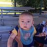 baby, child, infant, outdoor, picnic, picnic_table, bench, shelter, portrait, face, blue_eyes, sitting, bib, clothing, toy, adult, legs, trees, house, daylight
