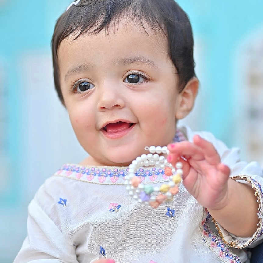 Ayzal Chaudhry is registered to the contest to win money with this photo: baby, background, beads, bracelet, child, clothing, colorful, cute, embroidered, face, fashion, hair_clip, hand, happy, jewelry, outdoor, person, portrait, smiling, toddler