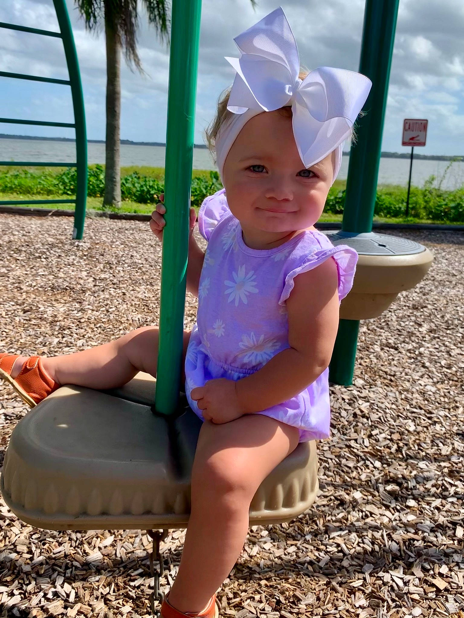 Gracie Mae is registered to the contest to win money with this photo: baby, child, city, fun, headgear, headwear, human_settlement, outdoor_play_equipment, person, plant, play, playground, public_space, purple, recreation, smile, summer, swing, toddler, tree