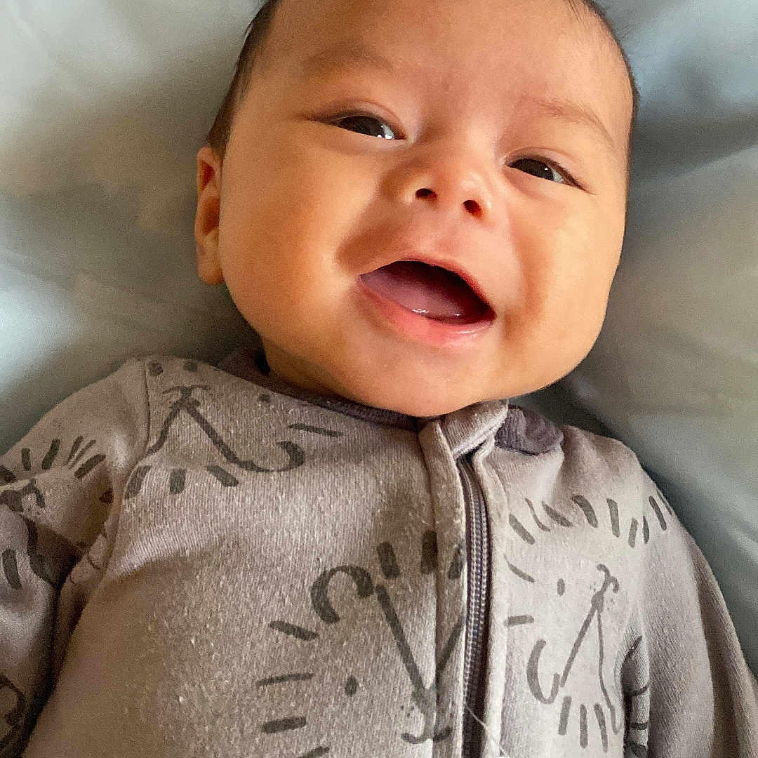 Lucas is registered to the contest to win money with this photo: baby, bed, blanket, child, clothing, comfort, cozy, cute, face, happy, indoors, infant, lying_down, onesie, portrait, sleepwear, smiling, soft, young, zipped