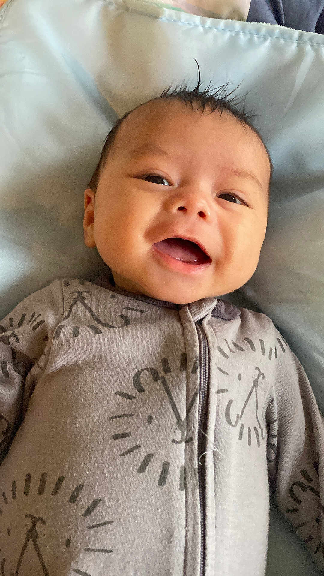 Lucas is registered to the contest to win money with this photo: baby, smiling, onesie, clothing, infant, face, happy, lying_down, blanket, bed, cute, child, portrait, young, sleepwear, cozy, indoors, comfort, zipped, soft