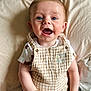 baby, child, smiling, happy, blue_eyes, overalls, checkered, white_shirt, bed, pillow, soft, cute, portrait, infant, hands, clothing, indoors, person, face, skin