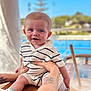 baby, child, smiling, blue_eyes, striped_clothing, knitwear, table, hand, tattoo, drink, straw, glass, outdoor, sunny, blurred_background, portrait, cute, happy, infant, person