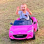 toddler, child, smiling, happy, toy_car, pink_car, outdoor, grass, hello_kitty, shirt, baby, playing, waving, summer, daylight, vehicle, fun, cute, portrait, young_child