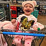toddler, child, shopping_cart, pink_clothing, hat, smiling, indoor, store, aisle, water_bottle, price_sign, toy, happy, cute, clothing, person, retail, baby, warm, fun