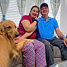 Athena joined the competition — help win amazing prizes! couple, smiling, golden_retriever, dog, indoor, couch, curtains, window, natural_light, casual_clothing, woman, man, pet, happy, relaxed, seated, living_room, home, paw, affection