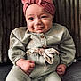 Ninon a rejoint le concours — aidez-le/la à gagner de superbes lots ! baby, child, headband, clothing, green_outfit, fist, smile, face, portrait, sitting, indoor, cute, infant, person, young, expression, fashion, cozy, background, texture