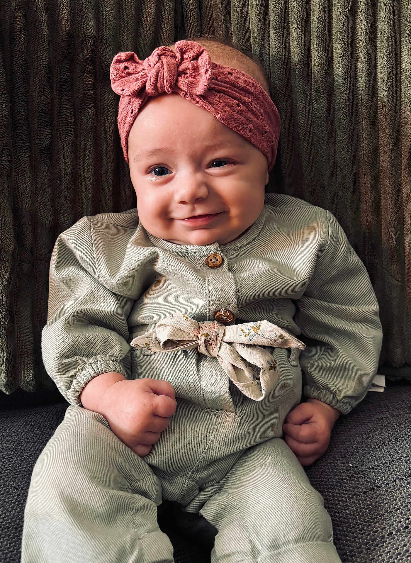 Ninon a rejoint le concours — aidez-le/la à gagner de superbes lots ! baby, child, headband, clothing, green_outfit, fist, smile, face, portrait, sitting, indoor, cute, infant, person, young, expression, fashion, cozy, background, texture