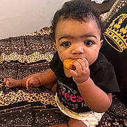 Grace joined the competition — help win amazing prizes! baby, infant, child, snack, food, bed, blanket, patterned_bedspread, pillow, crown_design, onesie, diaper, hands, face, eyes, sitting, indoor, portrait, cute, chewing