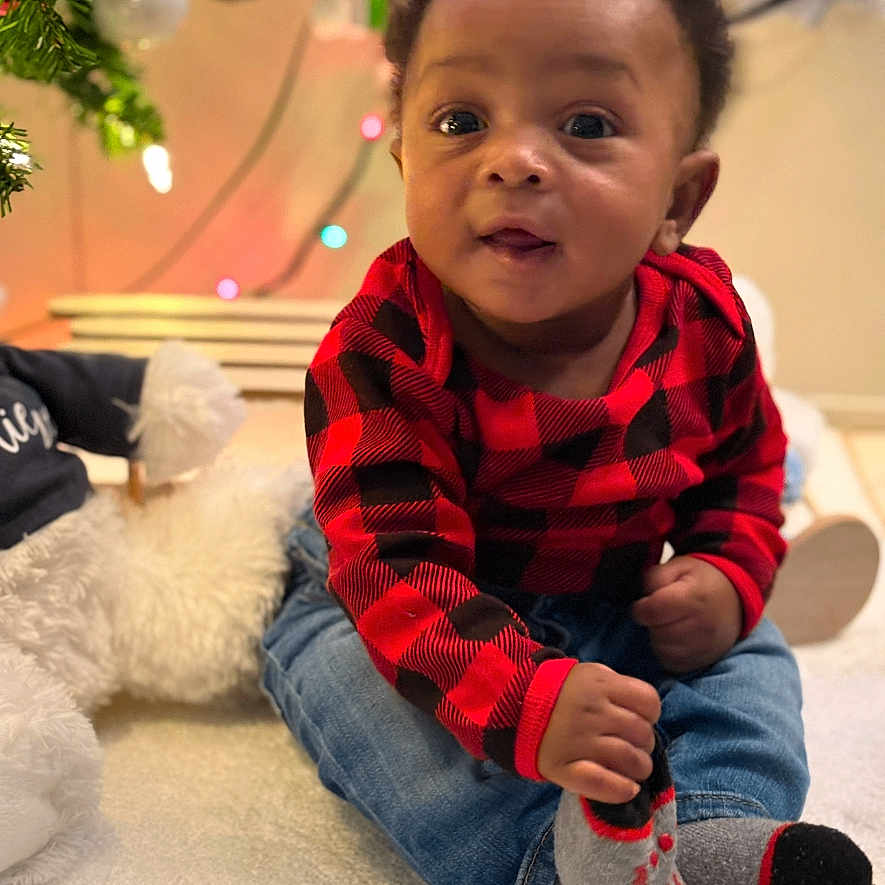 Lavell Faulkner is registered to the contest to win money with this photo: baby, checkered_shirt, child, christmas_tree, curious, cute, decorations, face, festive, holiday, holiday_lights, indoor, infant, jeans, red_shirt, sitting, smiling, sock, soft_surface, young_child