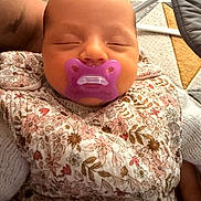 Léïa a rejoint le concours — aidez-le/la à gagner de superbes lots ! baby, infant, sleeping, pacifier, purple_pacifier, floral_clothing, blanket, swaddle, face, head, close_up, newborn, portrait, arm, adult_arm, indoor, tile_floor, carpet, cozy, soft_lighting