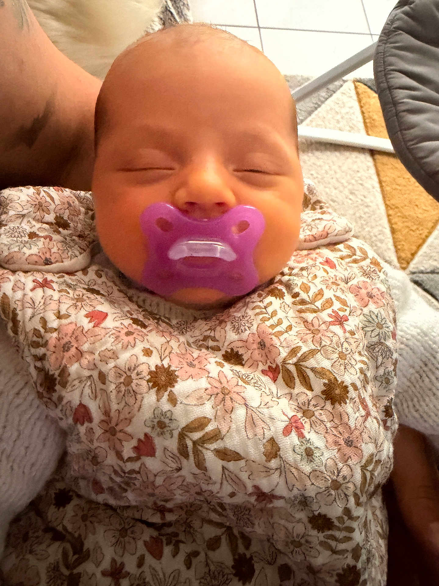 Léïa a rejoint le concours — aidez-le/la à gagner de superbes lots ! baby, infant, sleeping, pacifier, purple_pacifier, floral_clothing, blanket, swaddle, face, head, close_up, newborn, portrait, arm, adult_arm, indoor, tile_floor, carpet, cozy, soft_lighting
