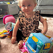 Isla joined the competition — help win amazing prizes! toddler, child, indoor, carpet, toy, colorful, blonde, curly_hair, blue_eyes, leopard_print, sitting, cute, playtime, living_room, couch, television, plastic_toy, soft_toy, foot, hand