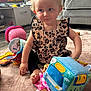 toddler, child, indoor, carpet, toy, colorful, blonde, curly_hair, blue_eyes, leopard_print, sitting, cute, playtime, living_room, couch, television, plastic_toy, soft_toy, foot, hand