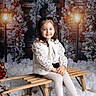 bench, brick_wall, child, coat, festive, garland, girl, holiday, lamppost, ornaments, pigtails, portrait, sitting, sled, smile, snow, studio_backdrop, white_tights, winter_scene, wreath