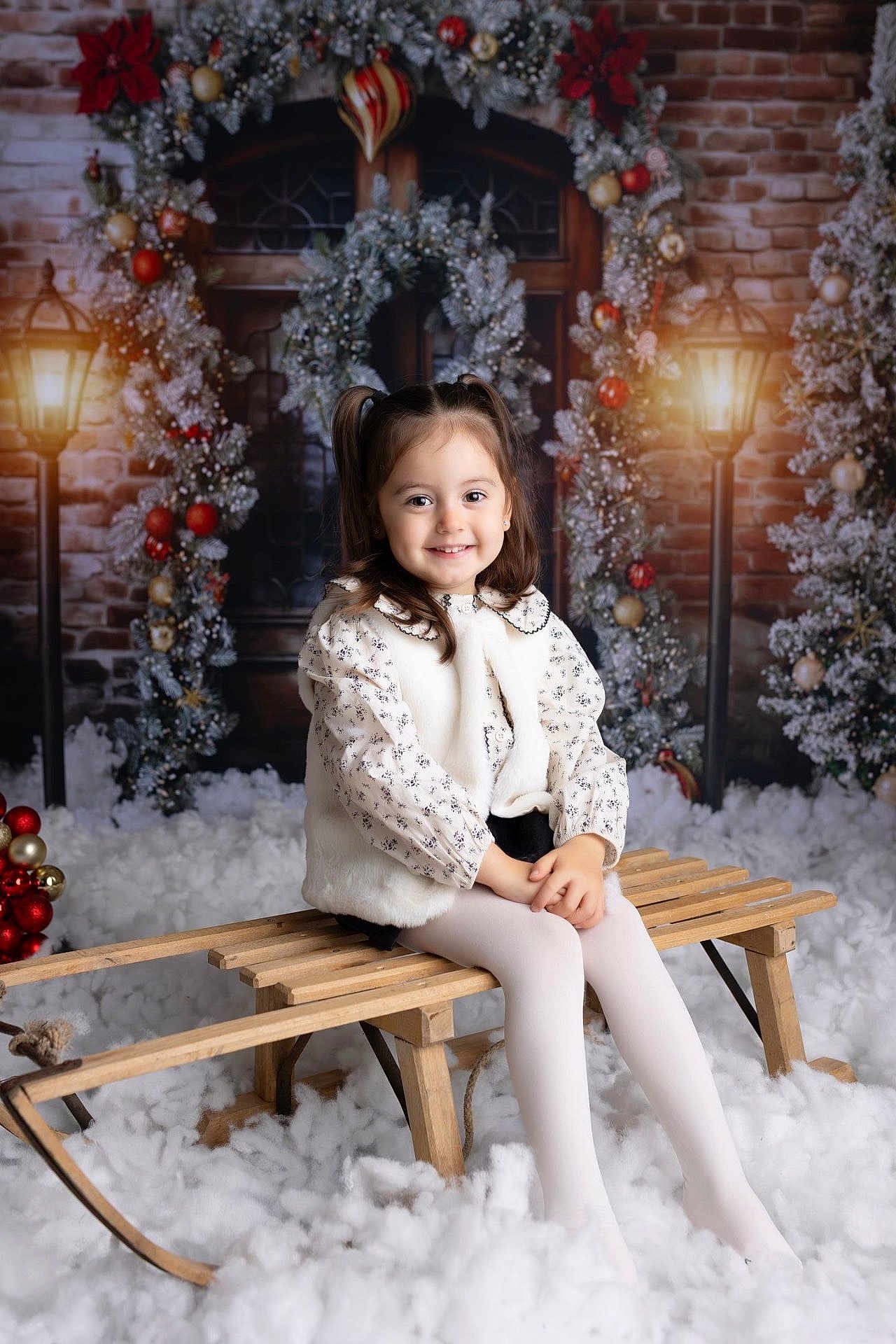 Luna participe au concours pour gagner de l'argent avec cette photo : child, girl, portrait, holiday, winter_scene, wreath, garland, ornaments, lamppost, sled, bench, snow, studio_backdrop, pigtails, smile, white_tights, coat, brick_wall, festive, sitting