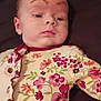 baby, child, face, eyebrows, floral, onesie, clothing, lying_down, infant, skin, expression, person, cute, young, portrait, indoor, fabric, pattern, sleepwear, head