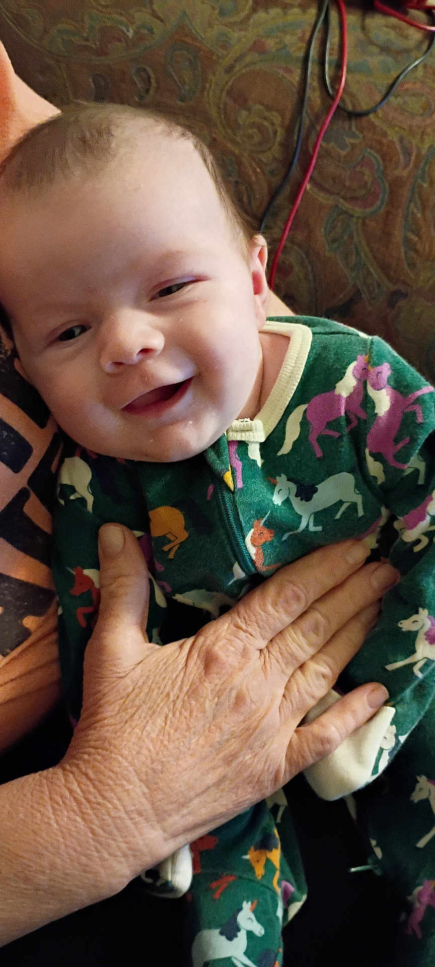 Morgan is registered to the contest to win money with this photo: baby, child, smiling, onesie, unicorn, hand, older_hand, patterned_clothing, portrait, indoor, person, cute, infant, holding, cozy, closeup, face, happy, apparel, resting