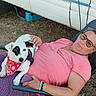 Hadès participe au concours pour gagner de l'argent avec cette photo : woman, dog, pet, outdoor, grass, chair, relaxing, pink_shirt, glasses, bandana, white_dog, black_patch, vehicle, leisure, casual, human, animal, friendship, summer, resting
