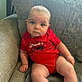 baby, child, infant, couch, sofa, red_clothing, onesie, sitting, indoor, curious, face, expression, quilted_cushion, window, daylight, skin, legs, hand, head, person