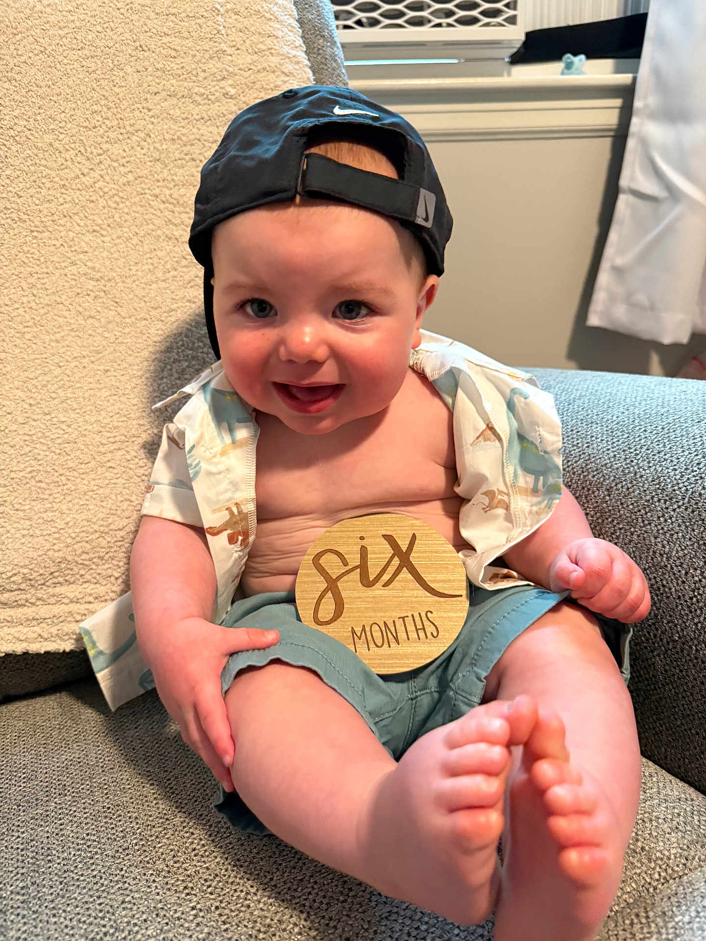 Jaxson joined the competition — help win amazing prizes! baby, infant, smiling, cap, shirt, shorts, wooden_sign, six_months, feet, toes, armchair, cozy, indoor, child, cute, happy, person, portrait, sitting, clothing