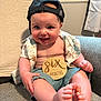 Jaxson is registered to the contest to win money with this photo: baby, infant, smiling, cap, shirt, shorts, wooden_sign, six_months, feet, toes, armchair, cozy, indoor, child, cute, happy, person, portrait, sitting, clothing