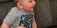 Jaxson is registered to the contest to win money with this photo: baby, child, couch, cute, expression, face, feet, gray, happy, head, indoor, infant, legs, person, portrait, shirt, sitting, skin, smiling, text