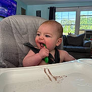 Jaxson joined the competition — help win amazing prizes! baby, chewing, child, couch, daytime, dog, furniture, high_chair, home, indoor, light, living_room, pattern, person, playful, seatbelt, smiling, spoon, television, window