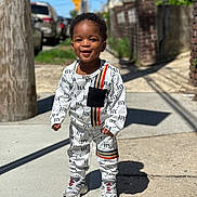 Kairo joined the competition — help win amazing prizes! toddler, child, smiling, standing, sidewalk, outdoor, sunny, street, clothing, sneakers, black_hair, brick_wall, utility_pole, shadow, casual, urban, happy, portrait, daylight, person
