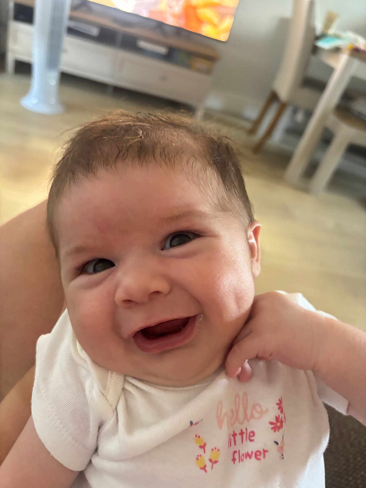Nyla joined the competition — help win amazing prizes! baby, smiling, face, infant, white_clothing, onesie, text, flower, hand, indoors, furniture, table, chair, floor, television, blurred_background, skin, cute, happy, person