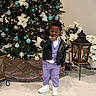 Joab is registered to the contest to win money with this photo: black_jacket, celebration, child, christmas_tree, contemplative, decor, festive, floor_tiles, holiday, holiday_decorations, indoor, lantern, lights, ornaments, person, poinsettia, purple_suit, standing, toddler, white_sneakers