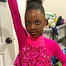 child, girl, pink_clothing, sequins, posing, indoor, portrait, afro_hair, confident, young, fashion, sparkle, long_sleeve, raised_arm, expression, person, room, door, blurred_background, standing