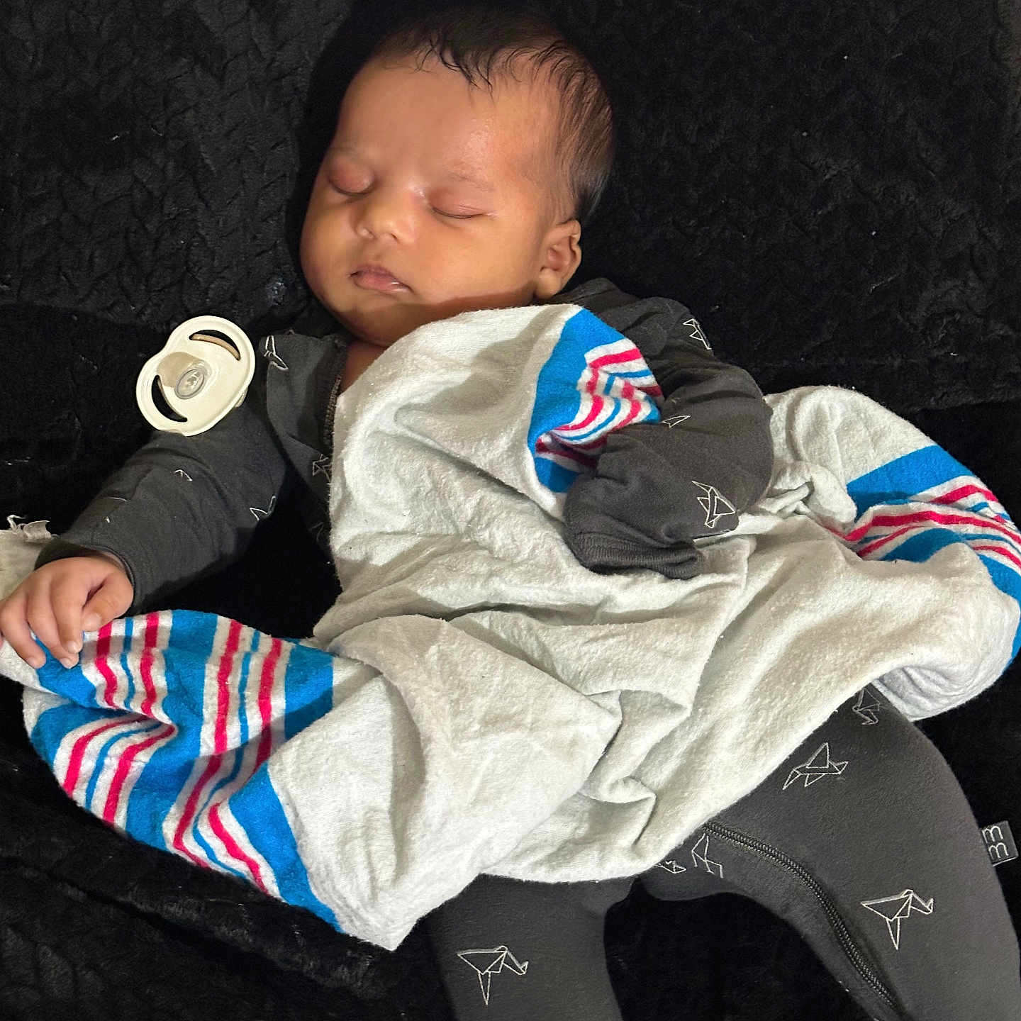 Chozen is registered to the contest to win money with this photo: baby, sleeping, blanket, pacifier, clothing, dark_background, cozy, infant, cute, resting, soft_texture, striped_blanket, peaceful, child, face, portrait, indoors, toddler, wearing, hands