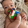 baby, blanket, chewing, child, closeup, couch, curious, cute, face, fingers, hand, indoor, infant, playful, relaxed, rubiks_cube, skin, soft_texture, toy, young