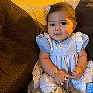 Melanie joined the competition — help win amazing prizes! baby, child, girl, dress, blue_dress, couch, bracelet, beads, necklace, indoors, portrait, cute, smiling, sitting, young_child, curly_hair, home, cozy, accessory, happy