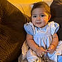 baby, child, girl, dress, blue_dress, couch, bracelet, beads, necklace, indoors, portrait, cute, smiling, sitting, young_child, curly_hair, home, cozy, accessory, happy