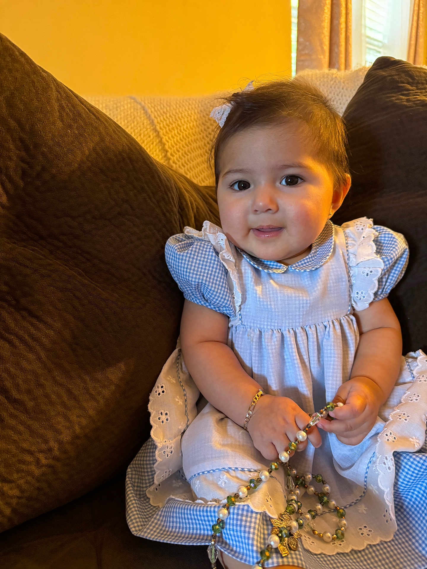 Melanie joined the competition — help win amazing prizes! baby, child, girl, dress, blue_dress, couch, bracelet, beads, necklace, indoors, portrait, cute, smiling, sitting, young_child, curly_hair, home, cozy, accessory, happy