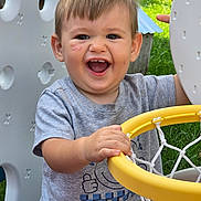 Ezra joined the competition — help win amazing prizes! toddler, child, smiling, happy, outdoor, basketball_hoop, playground, toy, plastic, grass, greenery, short_sleeve_shirt, scratches, face, person, play, daylight, casual_clothing, hand, young