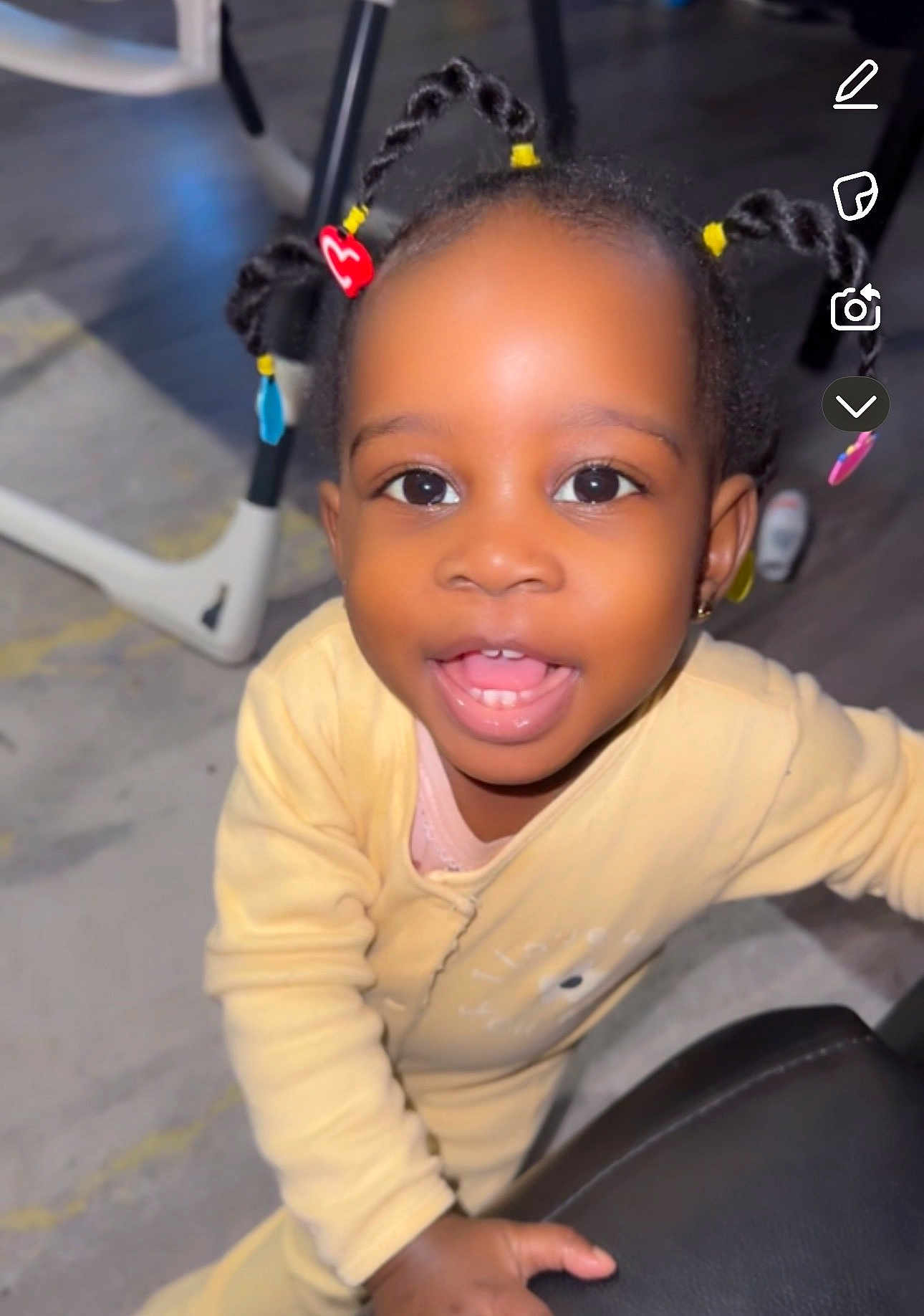 Kayla a rejoint le concours — aidez-le/la à gagner de superbes lots ! toddler, child, braided_hair, beads, yellow_clothing, indoor, smiling, happy, person, cute, baby, face, portrait, young_child, joyful, playful, hand, floor, furniture, closeup